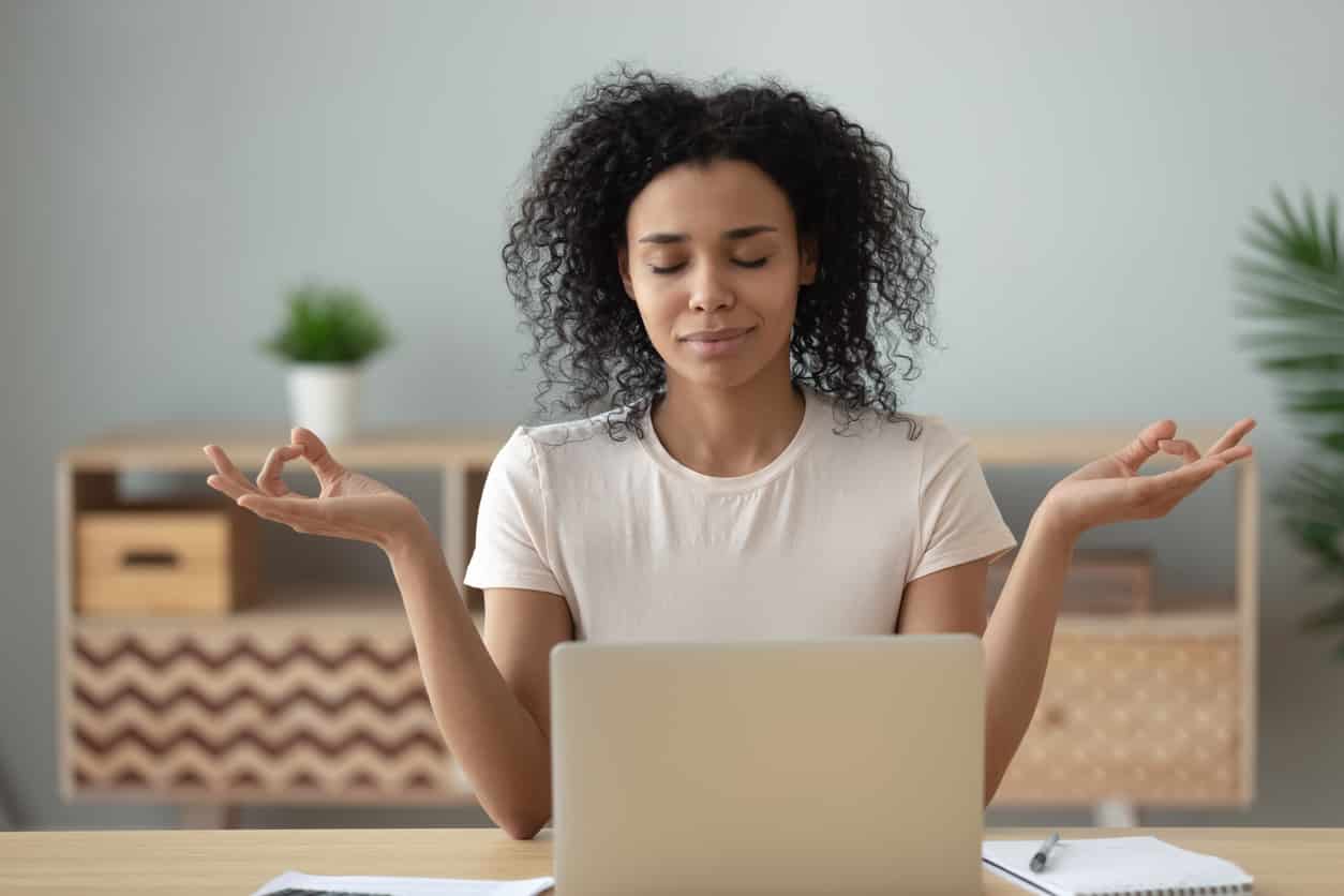 Woman meditating sitting at desk in front of laptop Woman meditating